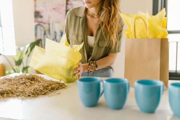 A Woman Wrapping a Mug with a Yellow Paper